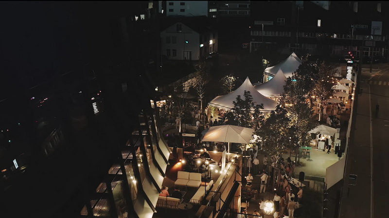 JED Park Der JED Park bei einer Abendveranstaltung mit leuchtenden Zeltdächern und vielen Menschen.